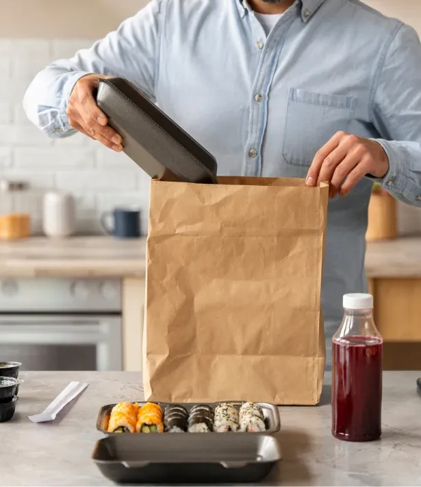 Person packing food into a bag with sushi and a drink nearby.